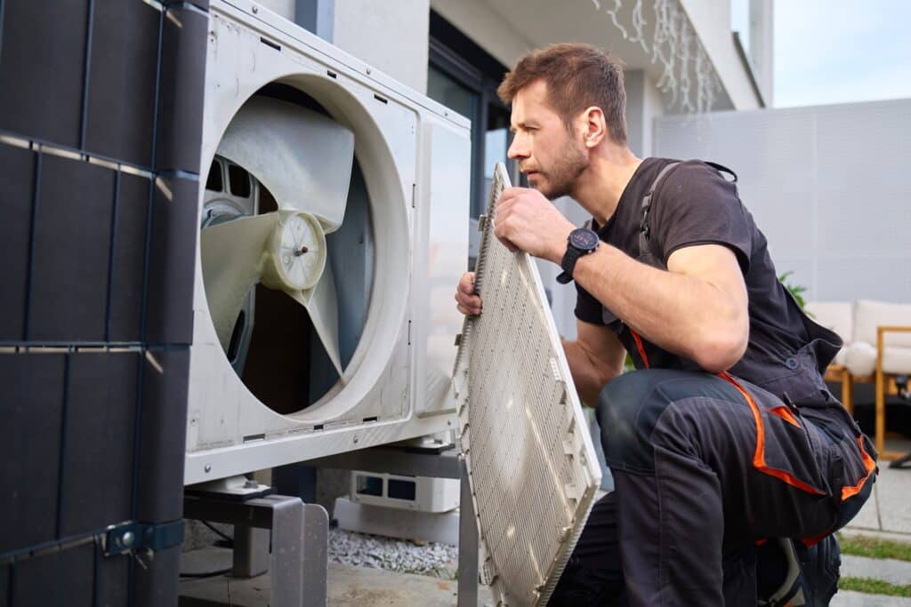 Technician removing front cover and inspecting fan inside outdoor heat pump unit.