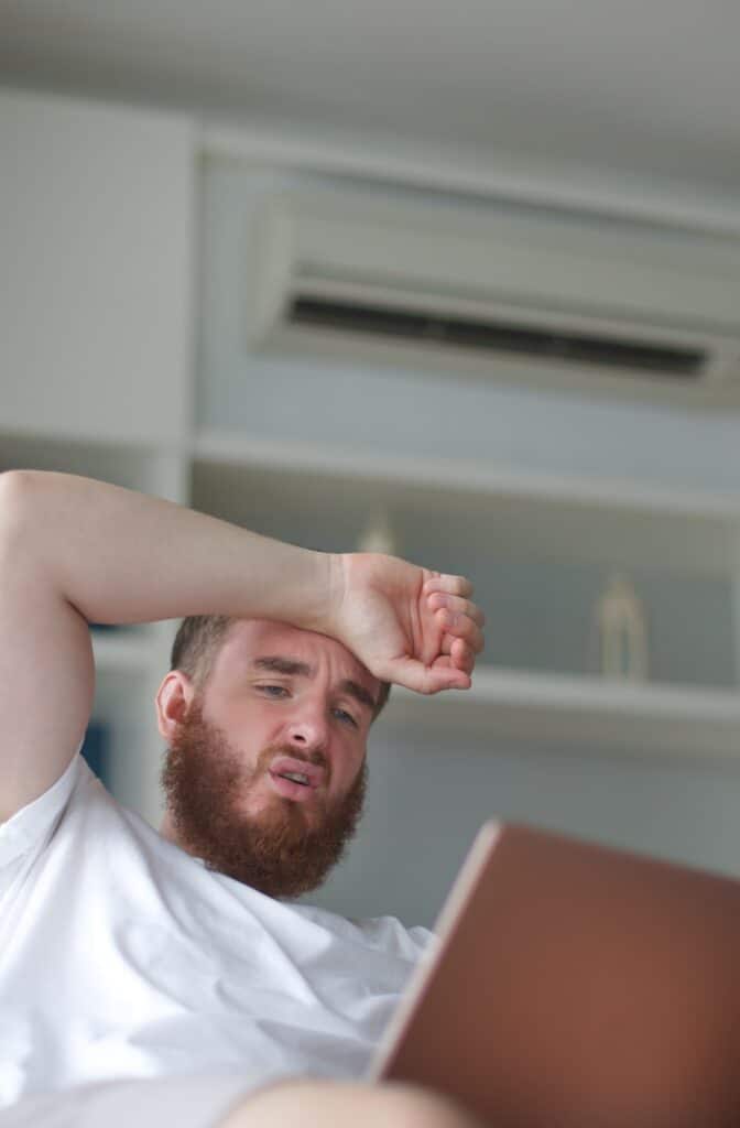 man sitting hot on couch because heat pump isn't working