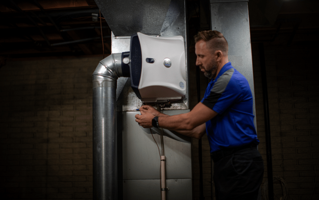 a man installing an AprilAire humidifier in a basement