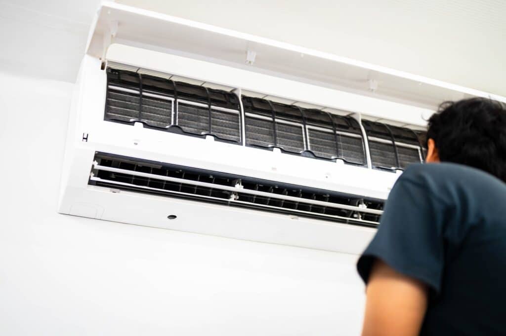 person in blue shirt looking up at heat pump unit on a white wall